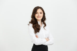 business concept: portrait confident young businesswoman keeping arms crossed and looking at camera while standing against grey background